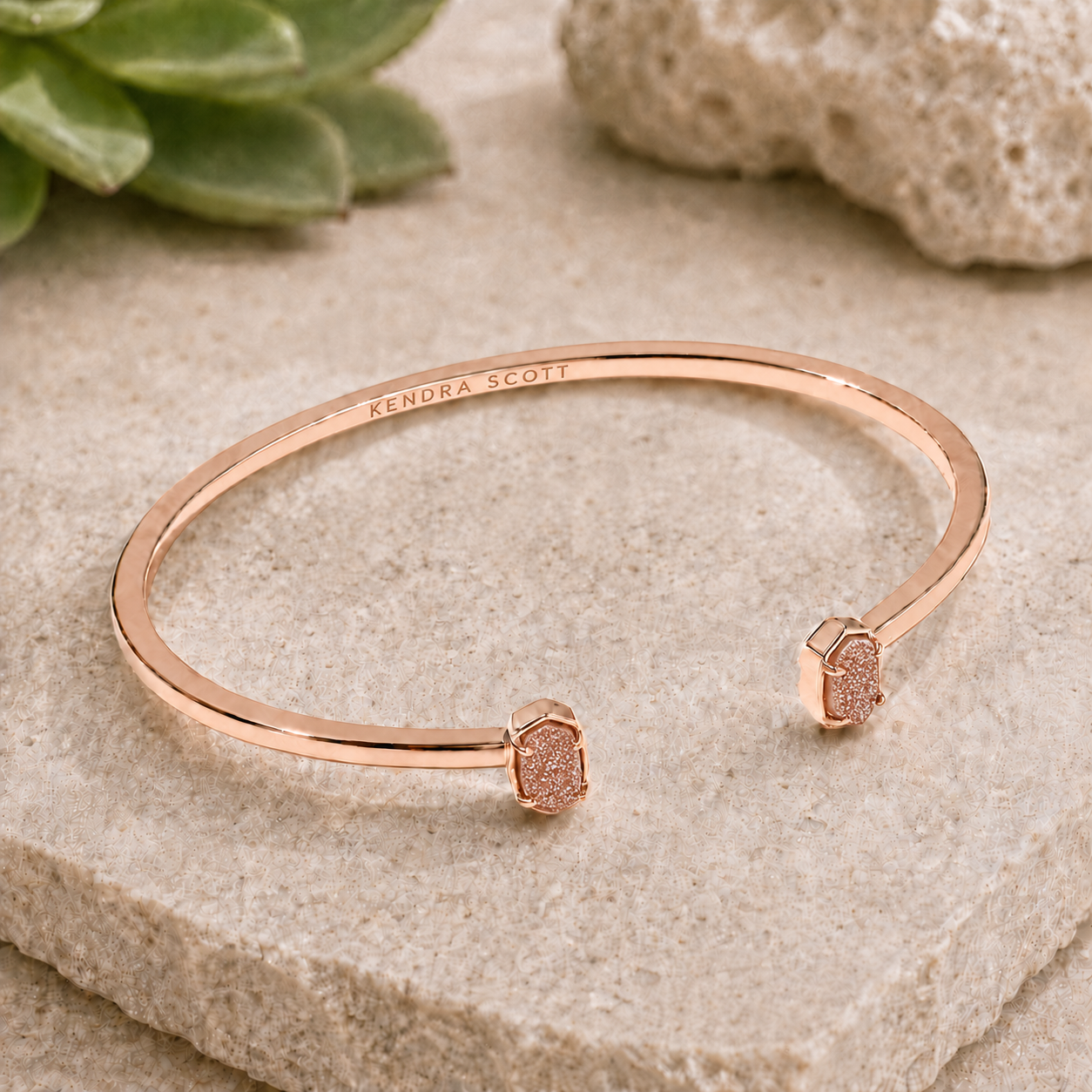 Kendra Scott Emilie rose gold Sand Drusy cuff bracelet on a textured neutral stone background