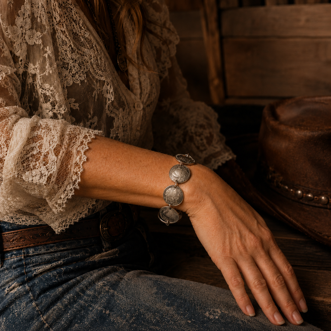 Western lifestyle image of a handmade Buffalo nickel coin bracelet worn on a model’s wrist with lace, denim, leather, and rustic wood details.