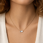 Woman wearing Kendra Scott Elisa Short Pendant Necklace in Gold Dichroic Glass with an iridescent oval pendant on a delicate gold chain